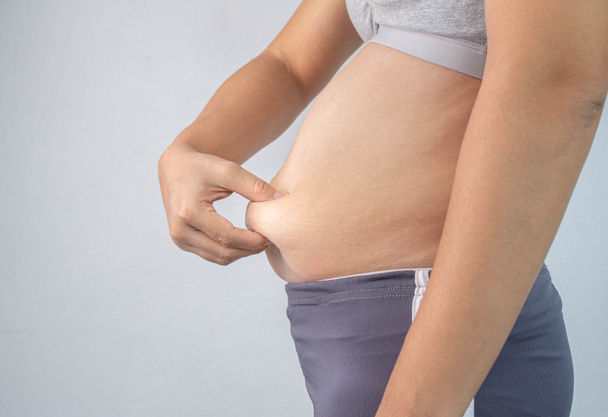 Lähikuva puolella näkymä naisen käsi puristamalla liiallinen vatsa rasvaa
  - Valokuva, kuva