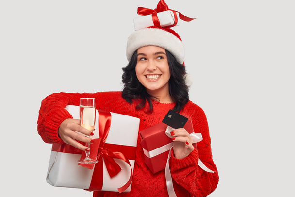 Kırmızı kazaklı güzel esmer kız ve elinde kırmızı kurdeleli beyaz hediye kutusu olan Noel Baba şapkası. - Fotoğraf, Görsel