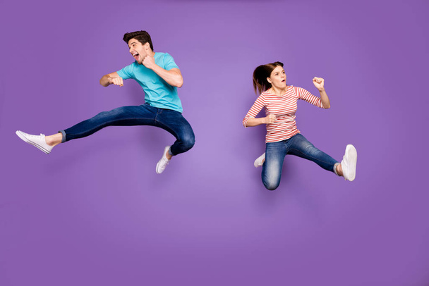 Full body photo of funny two people guy lady jumping high training fight club kicking leg wear casual blue striped t-shirts jeans footwear isolated purple color background - Fotoğraf, Görsel