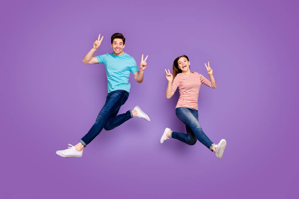 Full size profile photo of funky crazy two people guy lady jumping up high showing v-sign symbols wear casual blue striped t-shirts jeans shoes isolated purple color background - Foto, Imagem