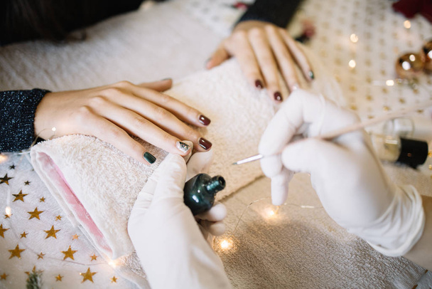 Close-up of manicurist painting Christmas tree on client nails - Fotó, kép