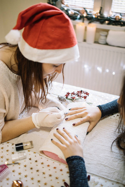 Manicurist with Santa hat doing manicure and painting nails - Фото, зображення