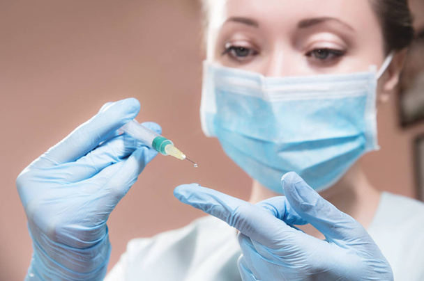 A professional cosmetologist doctor holds in his hand a syringe with anti-aging fluid. A hanging drop on the end of a needle with a filler over a gloved doctor finger. - Photo, Image