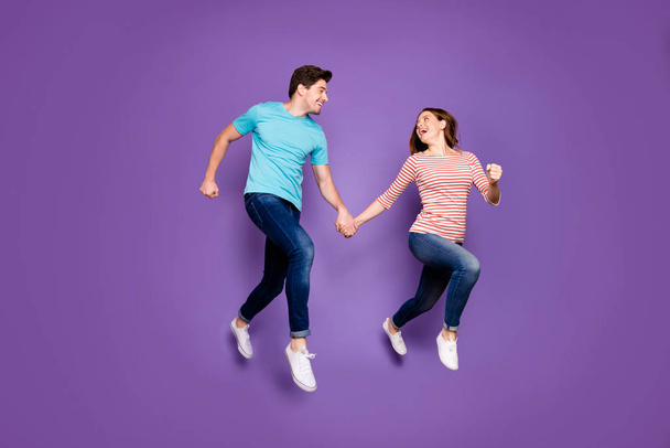 Full body profile photo of crazy funky two people guy lady jumping high rushing season sales black friday wear casual blue striped t-shirts jeans shoes isolated purple color background - Fotó, kép