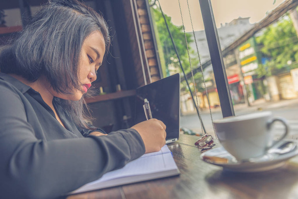 Freelance woman in black shirt writing next to laptop , coffee - Foto, afbeelding