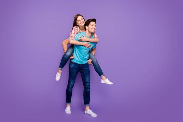 Full length photo of two carefree people guy carrying lady piggyback cheerful free time summer weekend wear casual stylish blue striped t-shirts jeans isolated purple color background - Foto, afbeelding