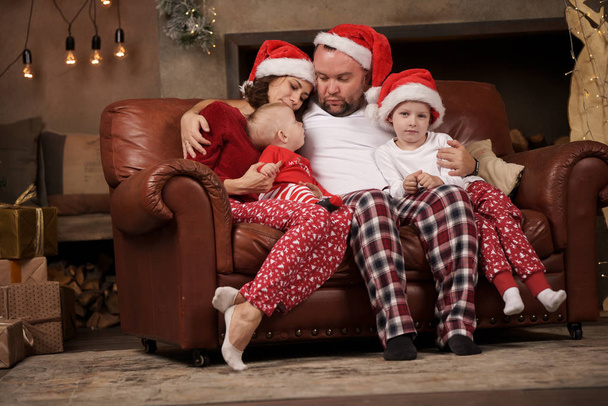 Image of happy parents in Santas caps and sons on leather sofa in studio - Foto, Bild