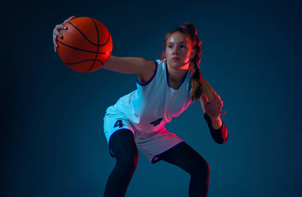 Young caucasian female basketball player on blue studio background in neon light - Фото, изображение