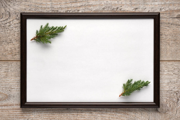 Photo frame with a sheet of white paper with copy space and Christmas tree branches inside on wooden surface. Flat lay, view from above, horizontal layout - Фото, изображение