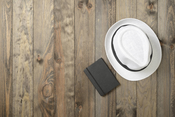 White hat and black notebook on wooden background - Foto, Bild