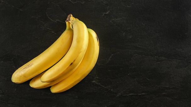 Top down view, bunch of yellow bananas on black board, space for - 写真・画像