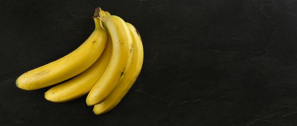 Top view, bunch of bananas on black stone board. Banner with cop - 写真・画像