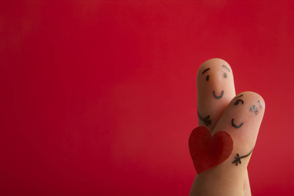 Walentynki zakochują się w koncepcji miłości. Malowane szczęśliwe śmieszne palce smiley trzymając czerwone serce na czerwonym tle z miejsca na tekst reklam - Zdjęcie, obraz