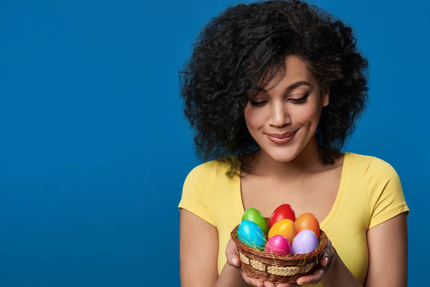 Smiling woman holding a basket with colorful Easter eggs - Foto, afbeelding