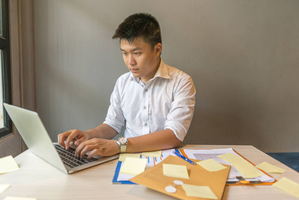 Young businessman working on laptop and reading financial report - 写真・画像