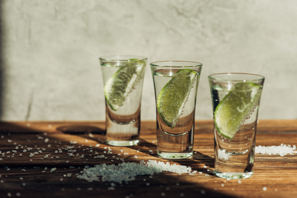 čerstvá tequila s vápnem a solí na dřevěném povrchu ve slunečním světle - Fotografie, Obrázek