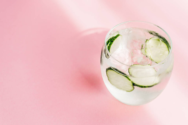 fresh lemonade with ice and cucumber slices on pink background with sunlight - Photo, image
