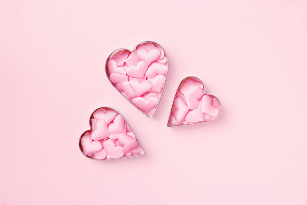 3 резака печенье в форме сердца с конфетти на пастельно-розовом фоне. Концепция валентинки. Вид сверху, пространство для копирования текста
. - Фото, изображение