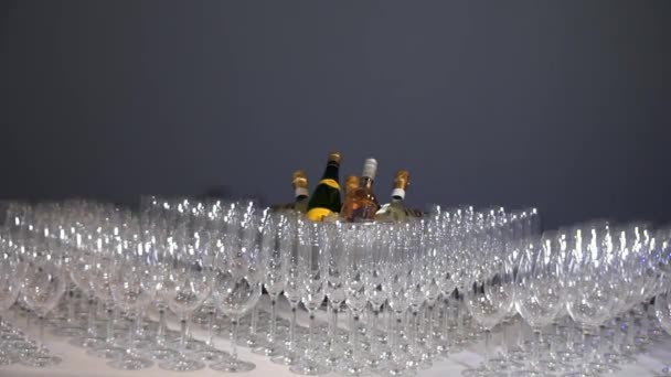 Πολλά γυάλινα ποτήρια λάμπουν στο τραπέζι του δείπνου στο φόντο του γκρίζου τοίχου. - Πλάνα, βίντεο