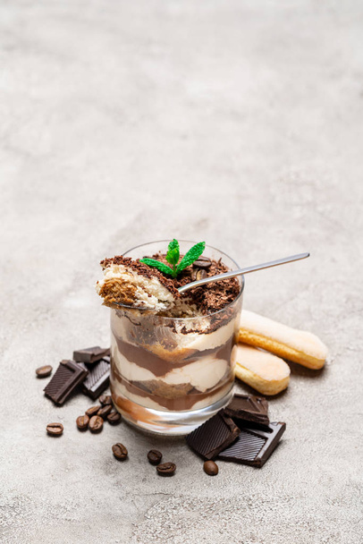 Classic tiramisu dessert in a glass cup, savoiardi cookies and pieces of chocolate on concrete background - 写真・画像