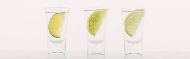 čerstvá tequila s vápnem v řadě izolované na bílém panoramatickém záběru - Fotografie, Obrázek