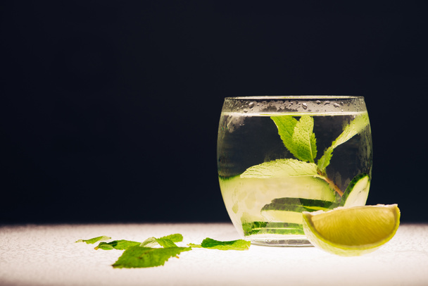 refreshing lemonade with mint, cucumber and lime on illuminated surface isolated on black - Foto, Imagen