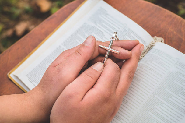 Mujer sosteniendo la cruz en la mano sobre el fondo de la Biblia
 - Foto, Imagen