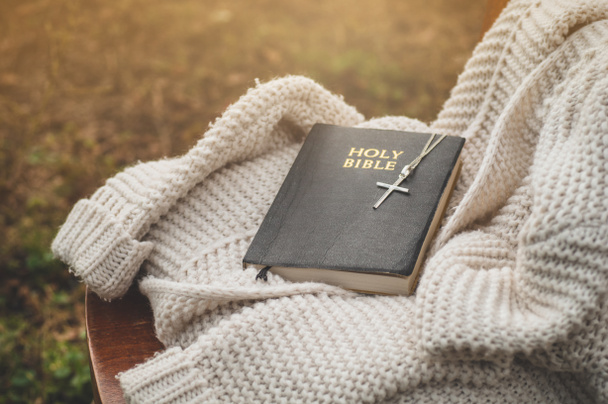 Biblia i krzyż leżą na ciepłym swetrze. Koncepcja wiary, duchowości i religii. - Zdjęcie, obraz