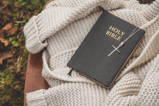De Bijbel en het kruis liggen op een warme trui. Concept voor geloof, spiritualiteit en religie. - Foto, afbeelding