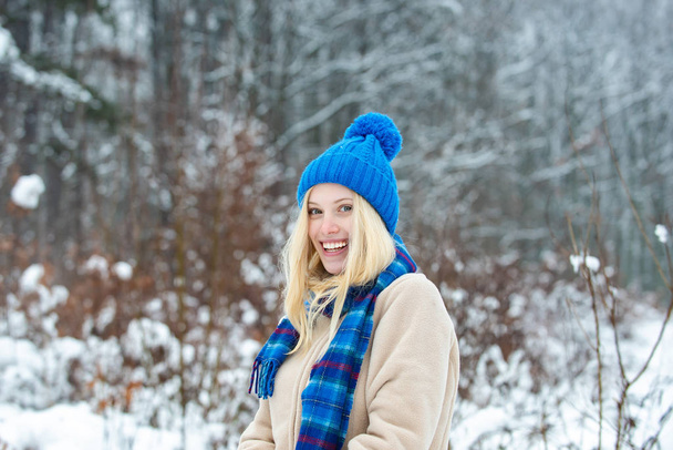 Красива блондинка в теплому блакитному капелюсі. Зимовий стиль для молодих жінок. Красива приваблива жіноча посмішка. Зимовий ліс і щасливий настрій у морозну погоду
. - Фото, зображення