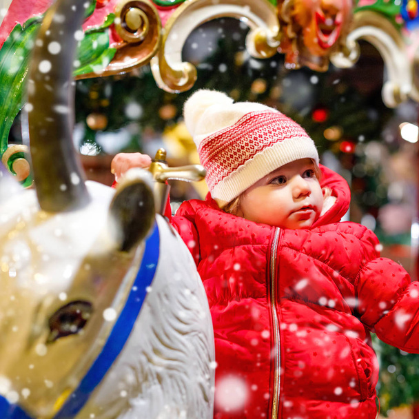 Adorable petite fille chevauchant sur un joyeux tour de cheval carrousel à la fête foraine de Noël ou au marché, en plein air. Happy enfant en bas âge s'amuser sur le marché de Noël familial traditionnel en Allemagne
 - Photo, image