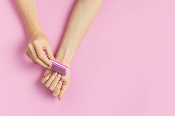 Stylish beautiful gentle manicure. Hands of young woman with nail file on pink background top view flat lay copy space. Natural nails, gel polish, self-care, beauty and fashion. Nail care salon spa - Foto, imagen