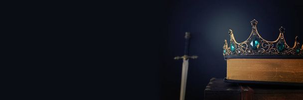 χαμηλή βασική εικόνα της όμορφης βασίλισσας / βασιλιά στέμμα πάνω από αντίκες βιβλίο δίπλα στο σπαθί. Φανταστική μεσαιωνική περίοδος. Επιλεκτική εστίαση - Φωτογραφία, εικόνα