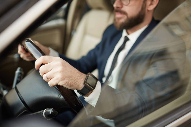 Jonge succesvolle zakenman in brillen en in pak zittend in luxe auto en rijdend  - Foto, afbeelding
