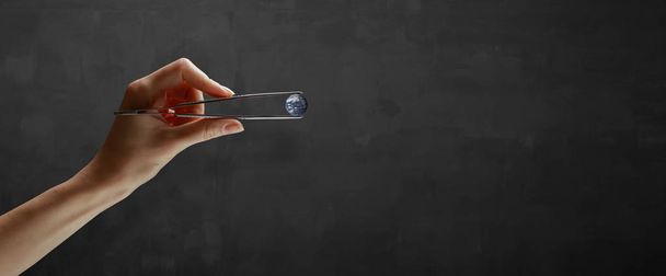 Hands holding planet in a tweezers over gray background - Photo, Image
