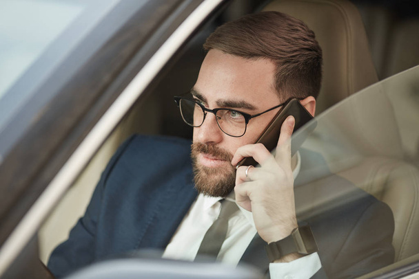 Young businessman in eyeglasses talking on mobile phone and driving the car  - 写真・画像