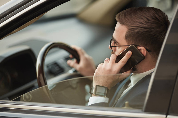 Νεαρός επιχειρηματίας με γυαλιά ηλίου που μιλάει στο κινητό τηλέφωνο και οδηγεί το αυτοκίνητο  - Φωτογραφία, εικόνα