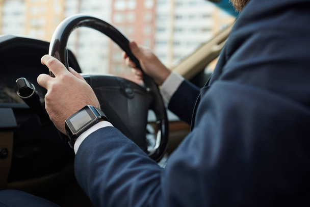 Close-up of man in suit holding wheel and driving car in the city - Photo, Image