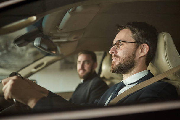 Двое молодых бизнесменов, сидящих в машине вместе на парковке, отправляются в командировку - Фото, изображение