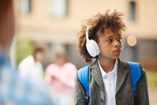 Afrikaanse schooljongen draagt koptelefoon luisteren naar muziek tijdens het lopen op straat na school - Foto, afbeelding