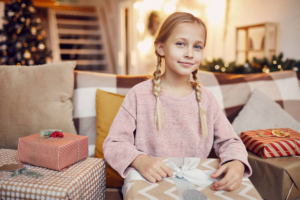 kleines Mädchen, das auf dem Sofa sitzt und große Weihnachtsgeschenke öffnet, die es vom Weihnachtsmann zu Weihnachten zu Hause bekommt  - Foto, Bild
