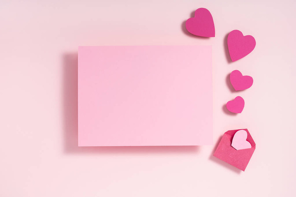バレンタインデーのフレーム構成。パステルピンクの背景に紙の紫色のピンクの心の空白のシート。トップビュー、フラットレイアウト、コピースペース - 写真・画像
