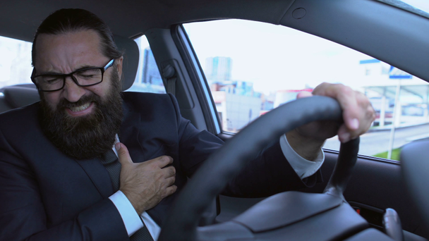 Vousatý muž v obleku trpí náhlou srdeční příhodou při řízení auta, stres - Záběry, video