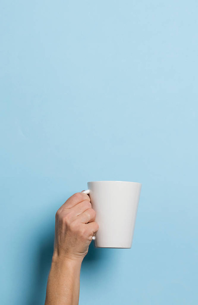 Frau hält eine Tasse Kaffee oder Tee auf blauem Hintergrund in der Hand. Food-Drink-Konzept. Kopierraum. - Foto, Bild