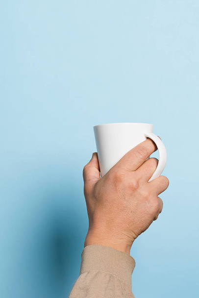 男は青い背景を手にコーヒーや紅茶を高く飲むのカップを保持します。フードドリンクのコンセプト。スペースのコピー - 写真・画像