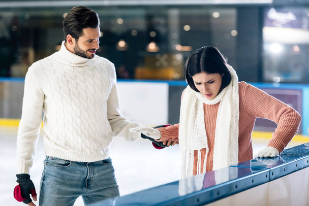 handsome man teaching girlfriend to skate on a rink while holding hands - Photo, Image
