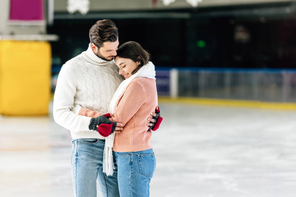young couple in sweaters hugging on skating rink  - Photo, Image