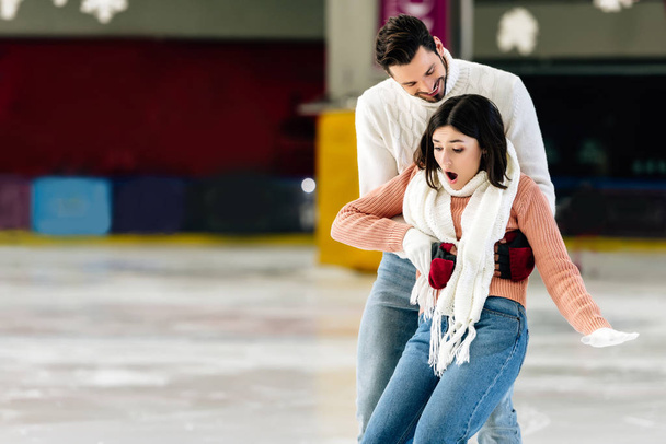 knappe man vangen bang vallende vrouw op schaatsbaan - Foto, afbeelding