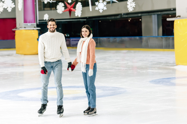 mosolygó fiatal pár kéz a kézben a korcsolyapályán   - Fotó, kép