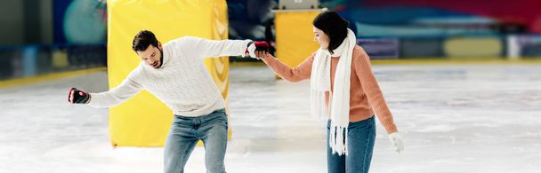 plano panorámico de la hermosa mujer joven enseñando al hombre a patinar en una pista de patinaje y de la mano
 - Foto, Imagen